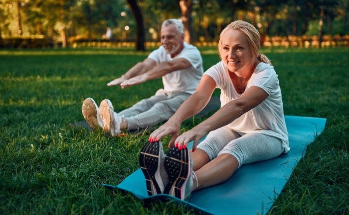 Natural Pharmaceuticals Movisan™ Collagen II Két idős felnőtt nyújtózik kint a parkban, jógaszőnyegen, napsütéses délutánon.